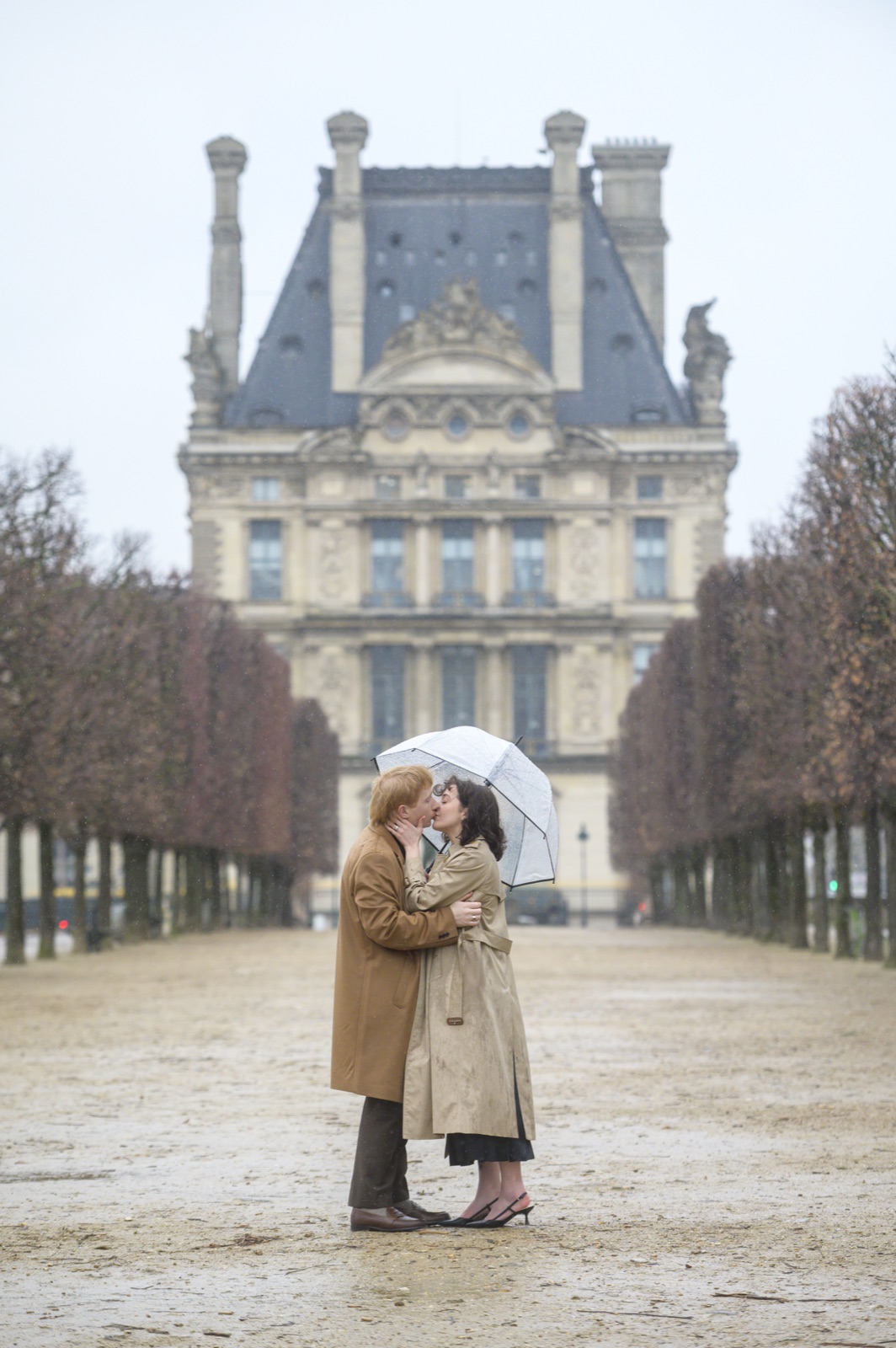 A newly engaged couple kissing beside the Louvre